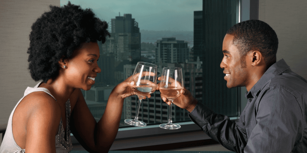 An African American couple cheers glasses of white wine.