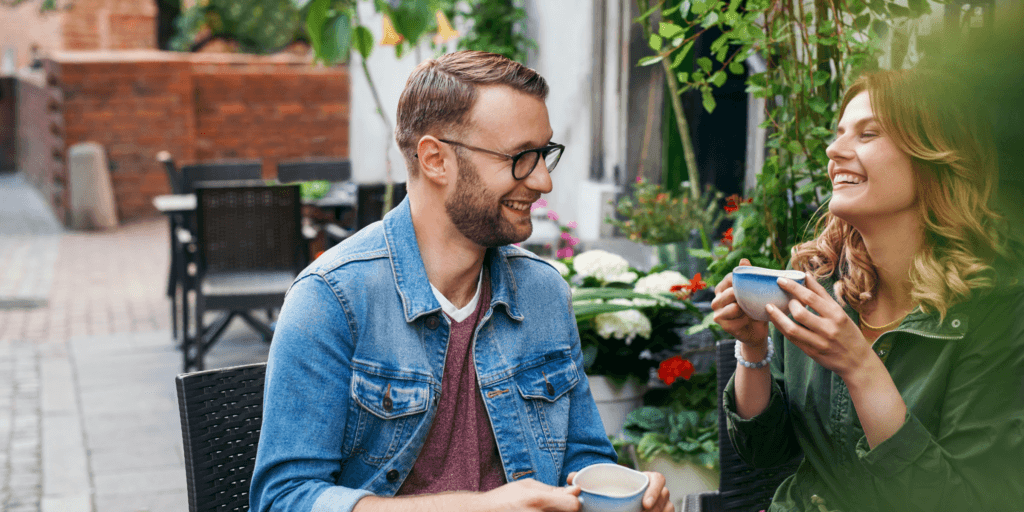 Signs of an emotionally available partner. A couple laugh over coffee drinks at a coffee shop.