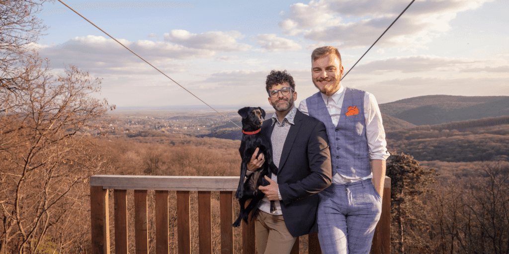 Generational differences are common for gay men who date as shown by this photo of a young gay man in a suit hugging an older gay man with a small black dog in his arms.