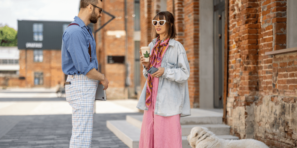 A man approaches a girl on the street as she drinks a coffee and shows body language that she may be interested in the man.