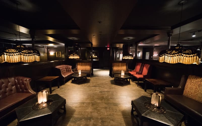 Interior of Carrie Nation cocktail club in Beacon Hill, Boston, with dim lighting, leather sofas, low tables with candles, and a long bar.