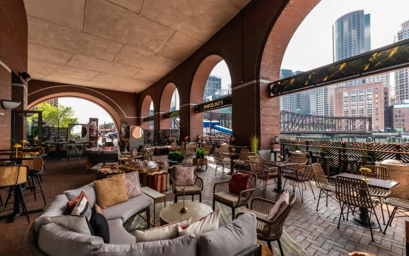 Covered arched patio of Marcelino's in Boston's Seaport, with lounge seating and cafe tables overlooking the city skyline and waterfront.