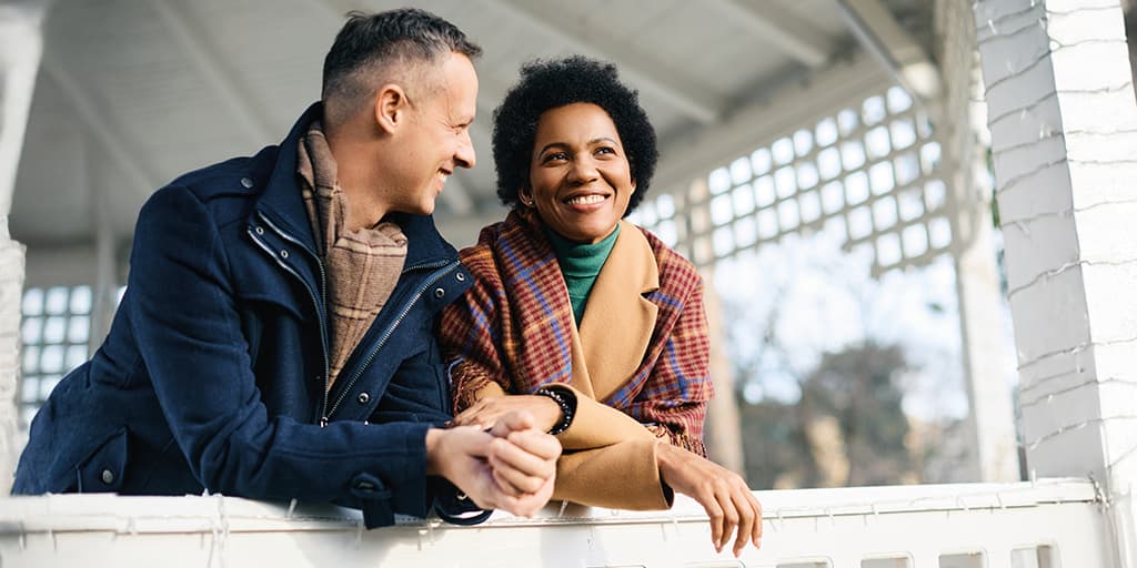 A happy couple lean on a railing happily talking on a date arranged by Tawkify matchmaking services.